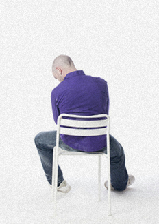 Depressed man hunched in chair, facing away and staring at the floor